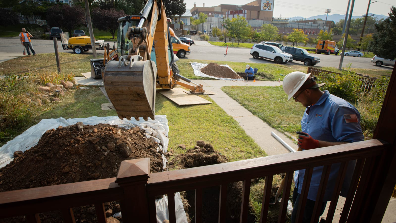 Excavator digging a trench in a front yard for a sewer line