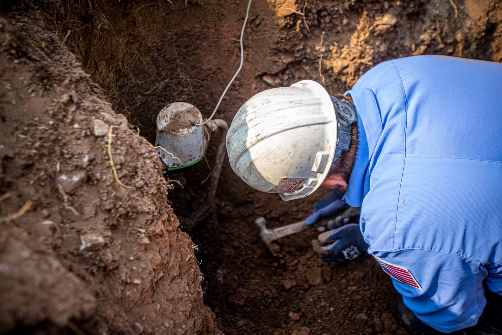Technician in a hard hat working on a water line in an excavated trench