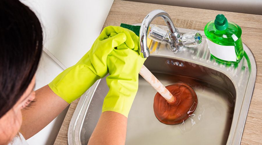 Woman unclogging sink drain with a plunger
