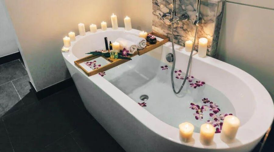 bath tub for spa, lit candles, flower peddles in water, tub tray across tub